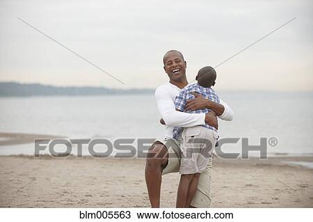 Stock Image - Black father and son hugging on beach. Fotosearch