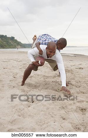 Stock Photo - Black father and son playing football at the beach. Fotosearch