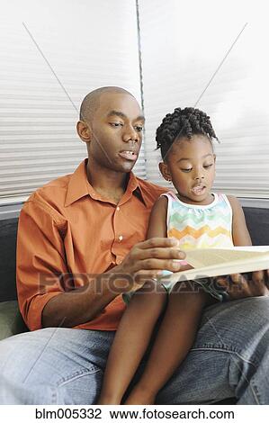 Stock Image - Black father reading book to daughter. Fotosearch