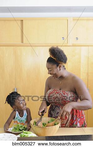 Stock Photo - Black girl with mother preparing salad in kitchen. Fotosearch