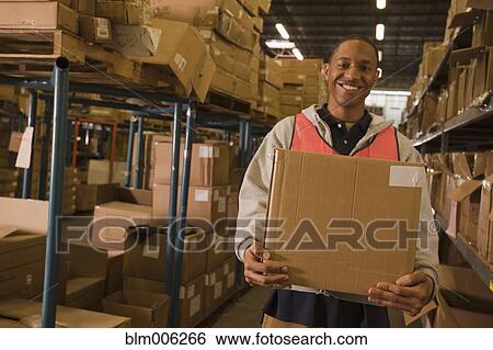 Stock Photograph - Black man carrying box in warehouse. Fotosearch
