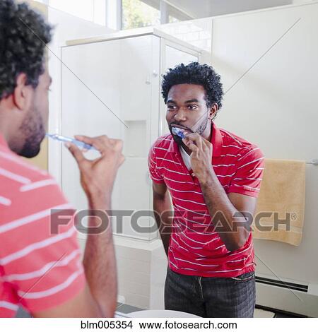 Picture - Black man in bathroom brushing teeth. Fotosearch