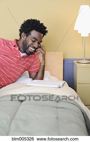 Stock Photograph - Black man in bedroom talking on cell phone. Fotosearch