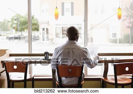 Stock Image - Black man reading paperwork in coffee shop. Fotosearch