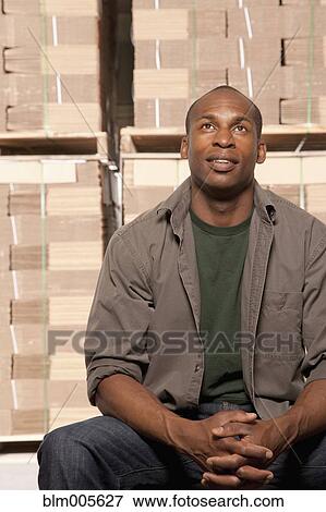 Stock Photo - Black man sitting in warehouse. Fotosearch