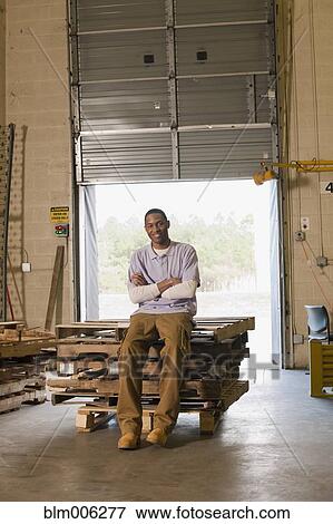 Stock Photo - Black man sitting on pallets in warehouse. Fotosearch