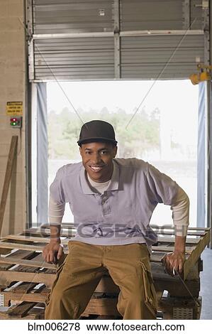 Stock Photo - Black man sitting on pallets in warehouse. Fotosearch