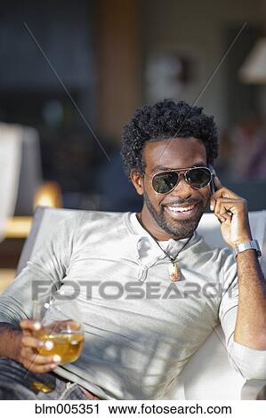 Stock Image - Black man talking on cell phone and drinking. Fotosearch