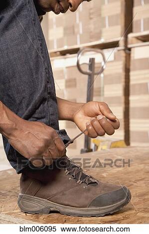Stock Photography - Black man tying shoes in warehouse. Fotosearch