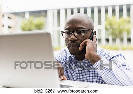 Stock Photo - Black man using cell phone and laptop outdoors. Fotosearch