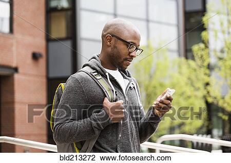 Stock Image - Black man using cell phone on city street. Fotosearch