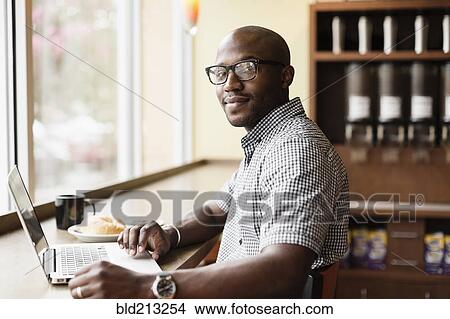 Picture - Black man using laptop in coffee shop. Fotosearch