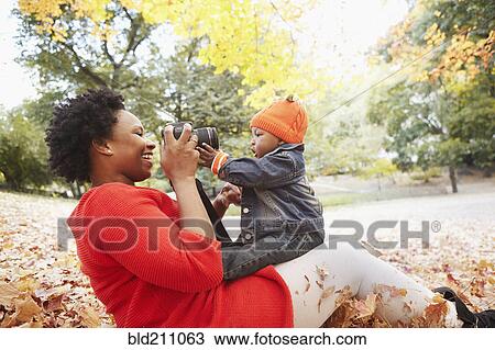 Stock Image - Black mother taking pictures of toddler son in park. Fotosearch