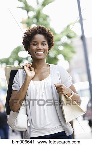 Stock Image - Black woman carrying shopping bags in city. Fotosearch
