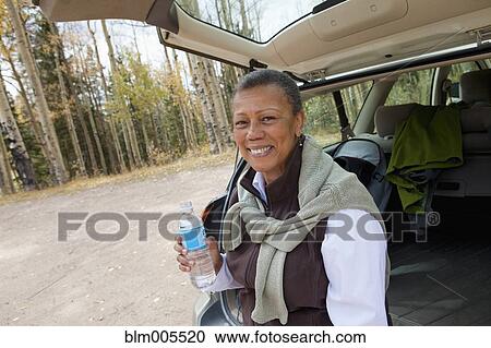 Stock Image - Black woman drinking water in back of car. Fotosearch
