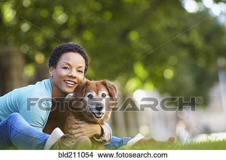 Picture - Black woman petting dog in park. Fotosearch