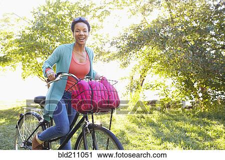 Stock Image - Black woman riding bicycle outdoors. Fotosearch