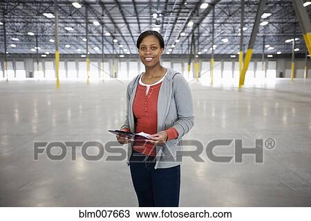 Stock Image - Black woman standing in empty warehouse. Fotosearch