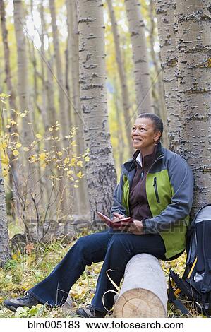 Stock Image - Black woman writing in diary in forest. Fotosearch