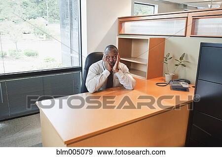 Stock Photo - Bored African businessman sitting at empty desk. Fotosearch