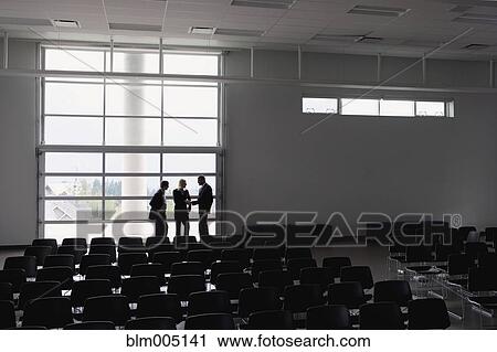 Stock Image - Business people talking in empty auditorium. Fotosearch