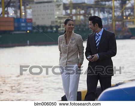 Stock Image - Businessman and businesswoman walking along waterfront. Fotosearch