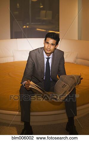 Stock Image - Businessman reading newspaper on round bed. Fotosearch