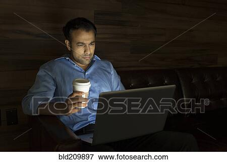 Stock Photo - Businessman using laptop on sofa at night. Fotosearch