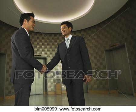 Businessmen shaking hands in office lobby View Large Photo Image Stock Photo - Businessmen shaking hands in office lobby. Fotosearch