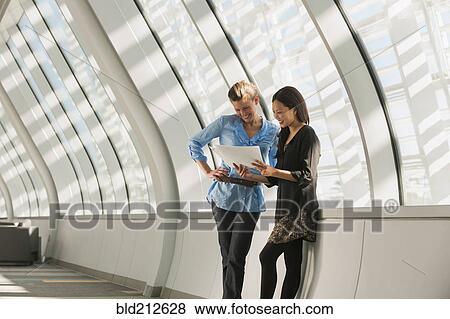 Stock Photo - Businesswomen reading paperwork in lobby. Fotosearch