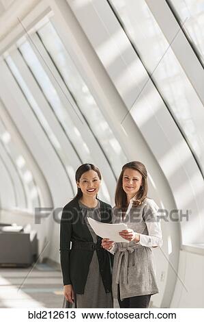 Stock Image - Businesswomen standing in lobby. Fotosearch