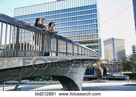 Stock Image - Businesswomen talking on urban sky bridge. Fotosearch