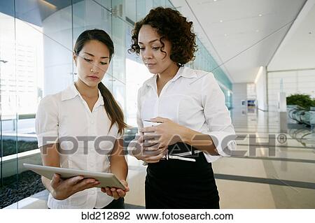 Stock Image - Businesswomen using tablet computer in lobby. Fotosearch