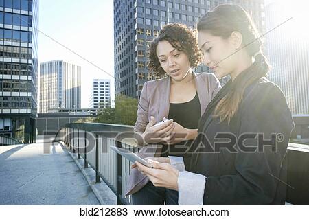 Stock Image - Businesswomen using tablet computer on urban sky bridge. Fotosearch