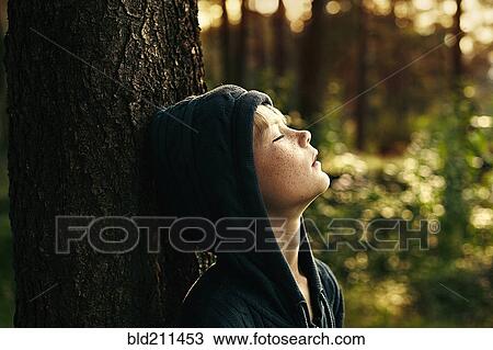 Stock Image - Caucasian boy leaning against tree. Fotosearch