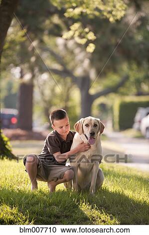 Stock Image - Caucasian boy petting dog in yard. Fotosearch