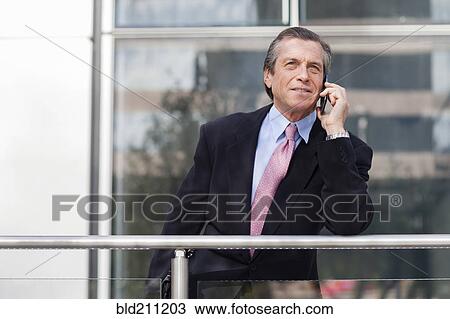 Stock Image - Caucasian businessman on cell phone on balcony. Fotosearch