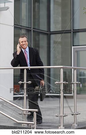 Picture - Caucasian businessman on cell phone outside building. Fotosearch