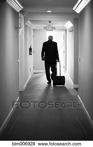 Stock Photo - Caucasian businessman pulling luggage in hotel hallway. Fotosearch