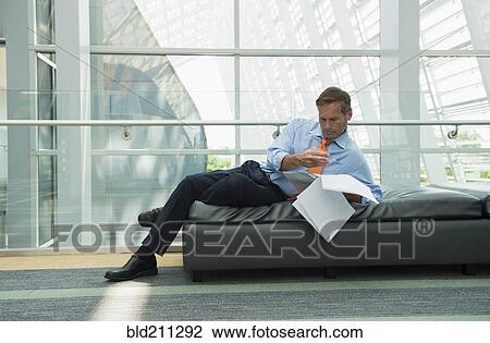 Stock Image - Caucasian businessman reading in lobby area. Fotosearch