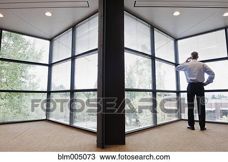 Stock Image - Caucasian businessman talking on cell phone in empty office. Fotosearch