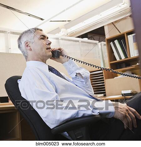 Caucasian businessman talking on phone at desk View Large Photo Image Stock Image - Caucasian businessman talking on phone at desk. Fotosearch