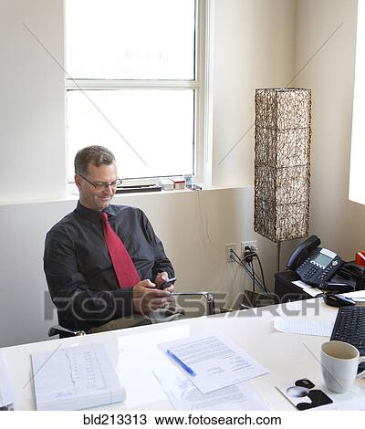 Stock Image - Caucasian businessman using cell phone in office. Fotosearch