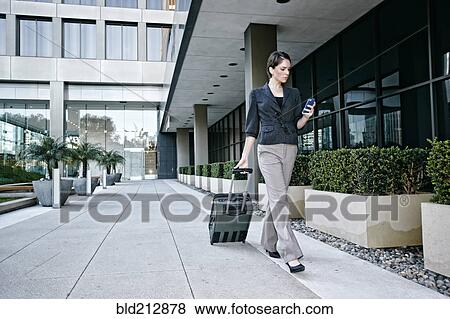 Stock Photo - Caucasian businesswoman rolling baggage outdoors. Fotosearch