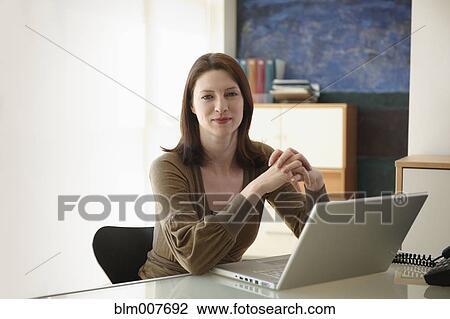 Stock Image - Caucasian businesswoman sitting at desk. Fotosearch