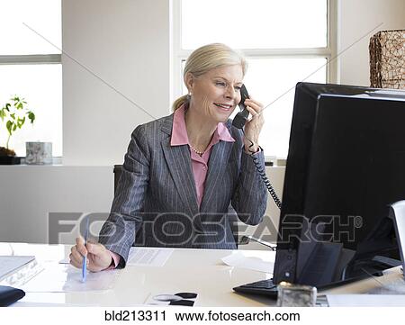 Stock Image - Caucasian businesswoman talking on phone at desk. Fotosearch