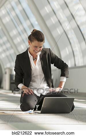 Stock Image - Caucasian businesswoman using laptop on lobby floor. Fotosearch