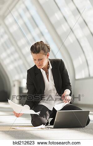 Stock Image - Caucasian businesswoman using laptop on lobby floor. Fotosearch