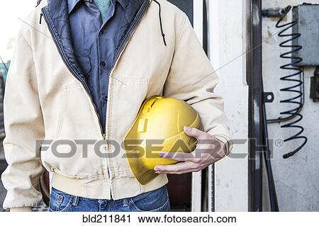 Stock Image - Caucasian construction worker holding hard-hat outdoors. Fotosearch