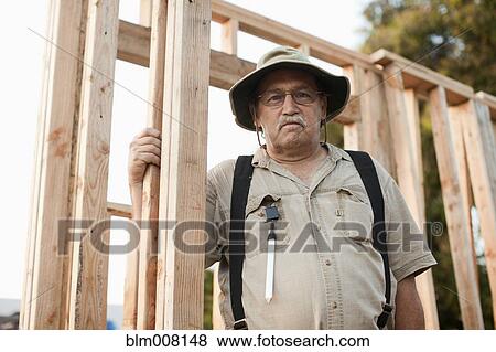 Stock Photo - Caucasian construction worker standing by house frame. Fotosearch